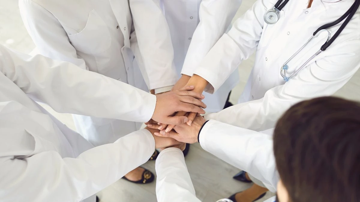Team di medici in camice bianco che uniscono le mani in segno di collaborazione